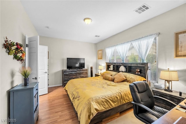 bedroom with baseboards, visible vents, and wood finished floors