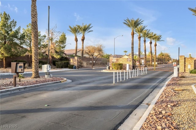 view of road featuring a gate, curbs, a gated entry, and street lights