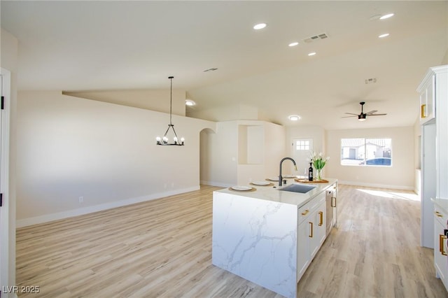 kitchen with a kitchen island with sink, a sink, white cabinets, open floor plan, and hanging light fixtures