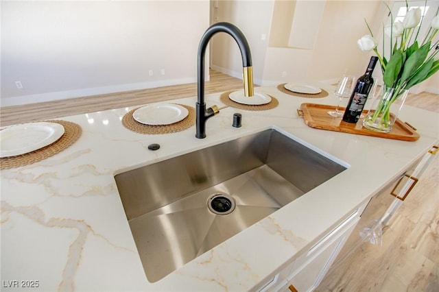 room details featuring light wood-style flooring, light stone counters, and a sink