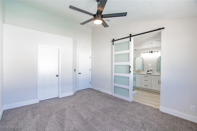 unfurnished bedroom with a barn door, baseboards, connected bathroom, light colored carpet, and a sink