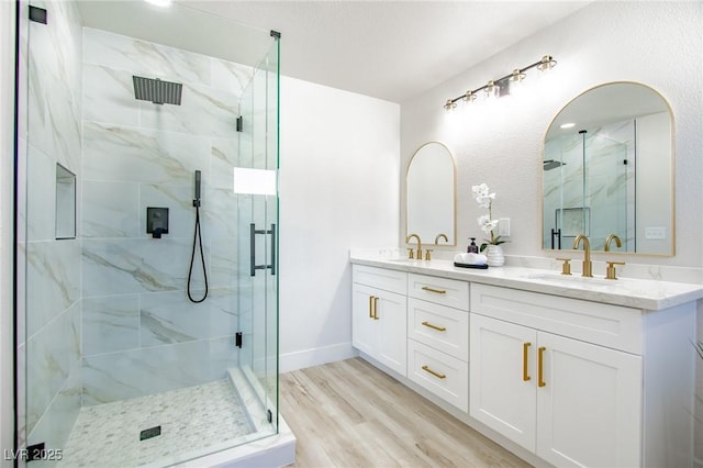 bathroom featuring double vanity, a marble finish shower, a sink, and wood finished floors