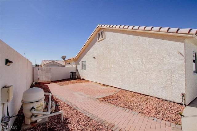 view of side of home with a fenced backyard, central AC unit, a patio, and stucco siding