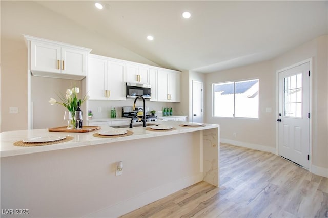 kitchen featuring vaulted ceiling, a kitchen island with sink, stainless steel microwave, and white cabinets