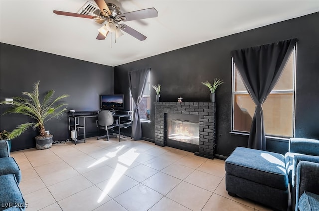 living room featuring a ceiling fan, an accent wall, a fireplace, and light tile patterned floors