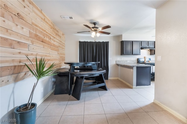 kitchen featuring ceiling fan, light stone counters, stove, wood walls, and visible vents