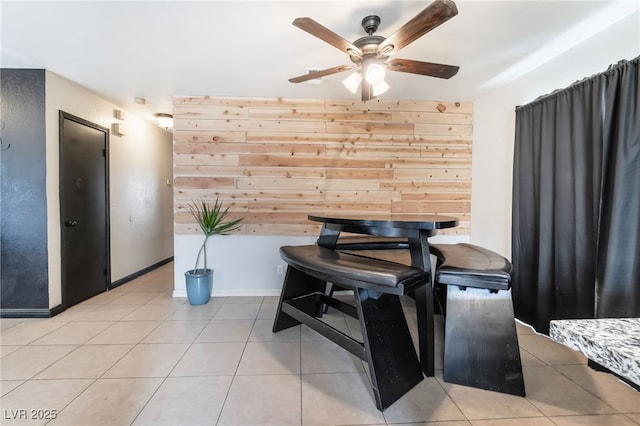 dining space featuring light tile patterned floors, ceiling fan, baseboards, and wood walls