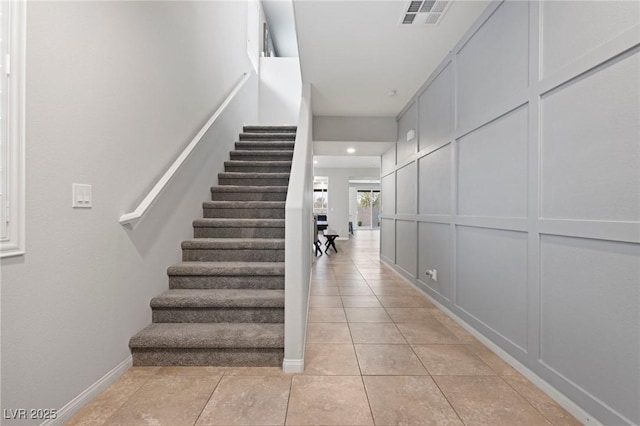 stairs with tile patterned floors, a decorative wall, baseboards, and visible vents