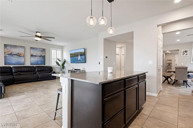 kitchen featuring light tile patterned floors, light stone countertops, a breakfast bar, decorative light fixtures, and open floor plan