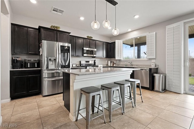 kitchen featuring a kitchen bar, visible vents, a sink, a kitchen island, and stainless steel appliances