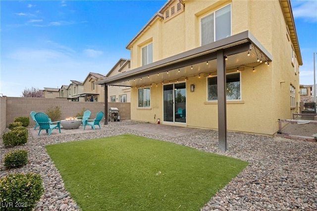 rear view of property featuring stucco siding, a patio, an outdoor fire pit, and a fenced backyard