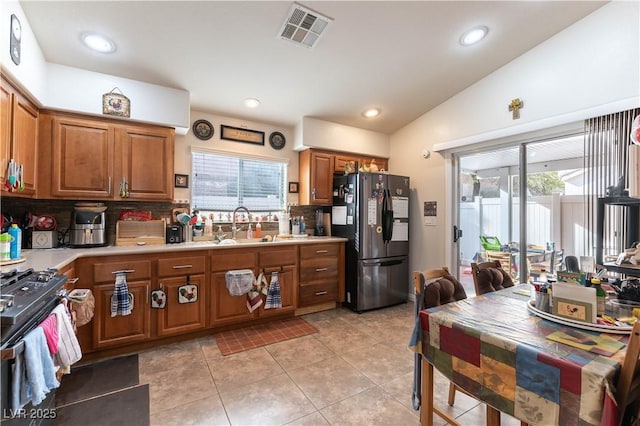 kitchen with visible vents, brown cabinetry, gas range, freestanding refrigerator, and vaulted ceiling