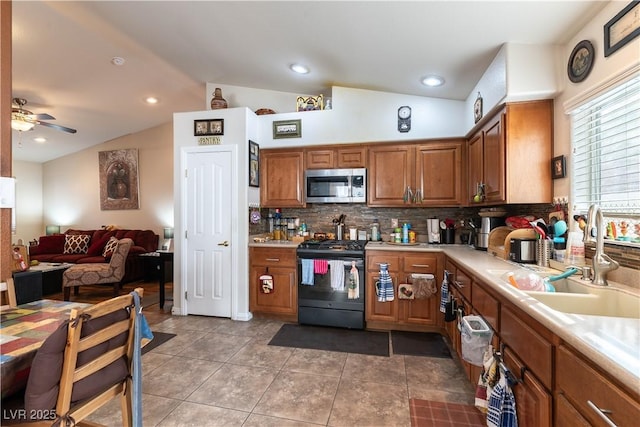 kitchen with brown cabinets, lofted ceiling, appliances with stainless steel finishes, a ceiling fan, and a sink