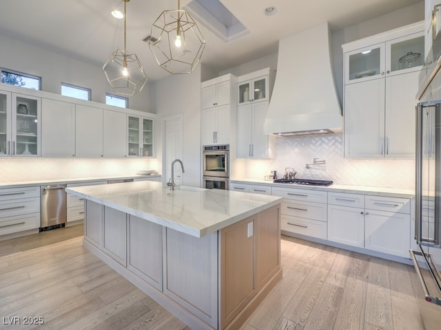 kitchen featuring a kitchen island with sink, custom exhaust hood, and glass insert cabinets