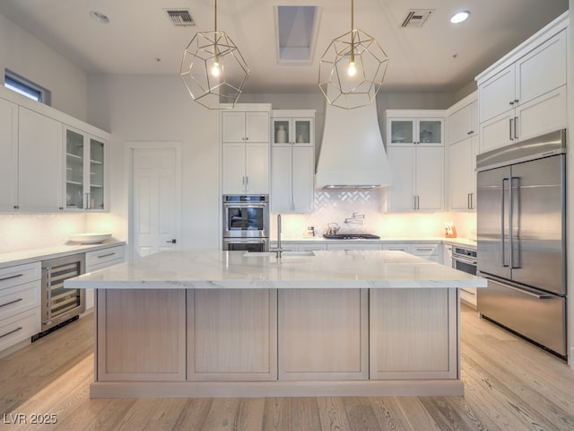 kitchen featuring a center island with sink, visible vents, appliances with stainless steel finishes, light stone countertops, and beverage cooler