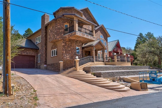 view of front of house featuring a garage, concrete driveway, a chimney, and a balcony