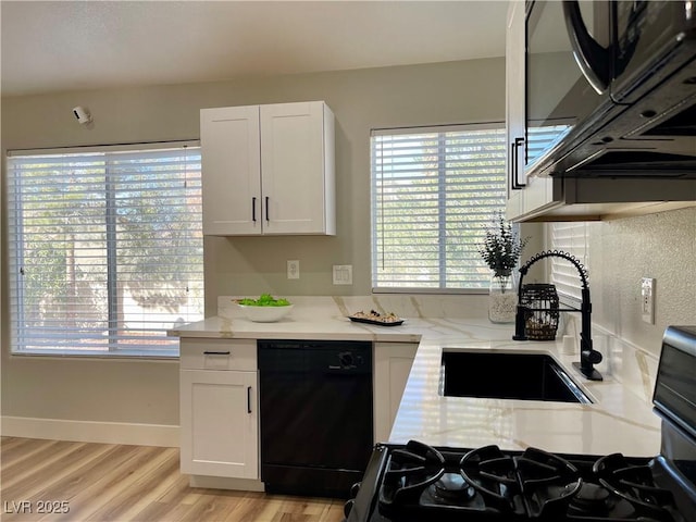 kitchen with light wood-style floors, white cabinetry, a sink, light stone countertops, and black appliances