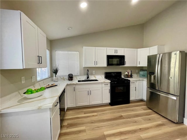 kitchen with light stone counters, light wood finished floors, white cabinets, a sink, and black appliances