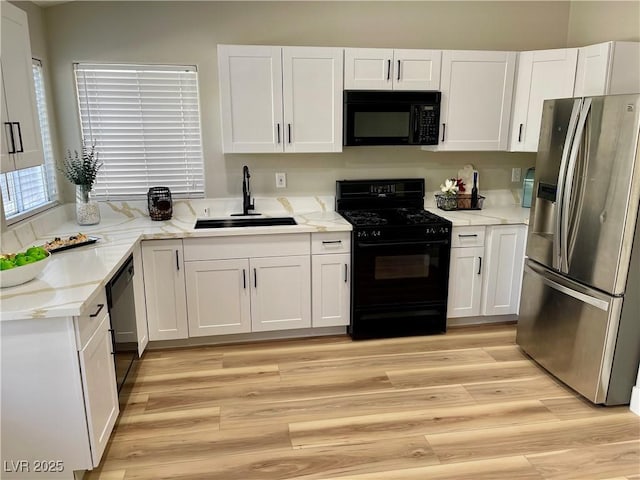 kitchen with light stone counters, a sink, white cabinets, black appliances, and light wood finished floors