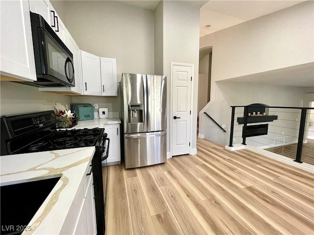 kitchen featuring light wood-style floors, white cabinets, a sink, light stone countertops, and black appliances