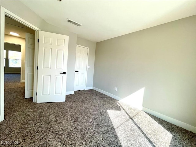 unfurnished bedroom with dark colored carpet, visible vents, and baseboards