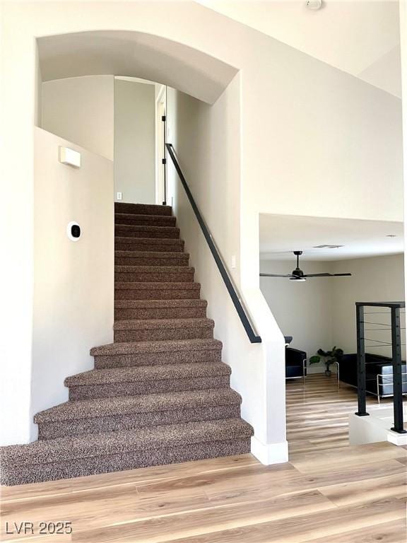 staircase featuring ceiling fan, arched walkways, and wood finished floors