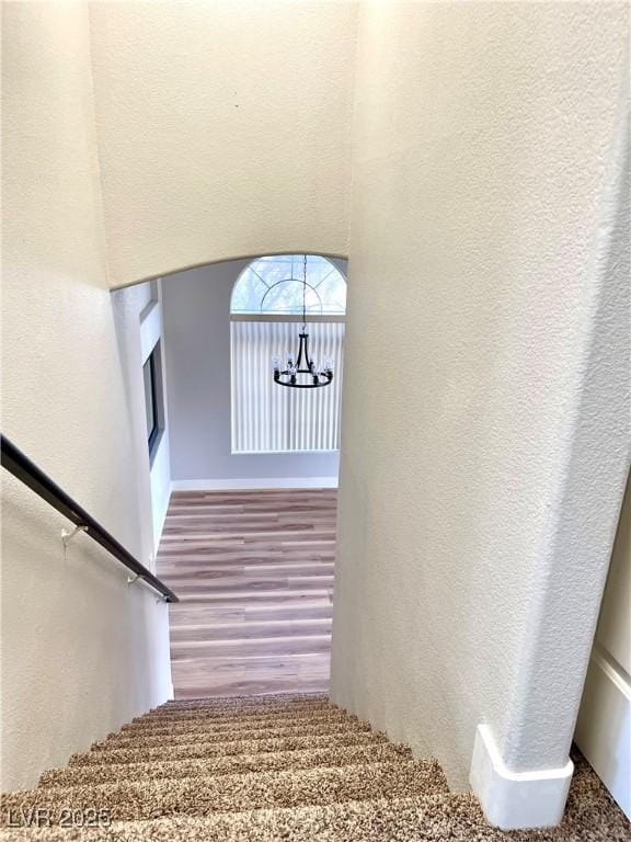 stairs featuring wood finished floors, a textured wall, and an inviting chandelier