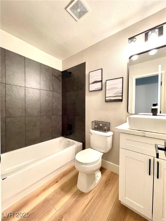 bathroom featuring a textured ceiling, shower / bathtub combination, toilet, wood finished floors, and visible vents