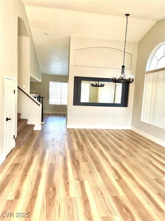 unfurnished living room featuring a notable chandelier, wood finished floors, baseboards, vaulted ceiling, and stairs