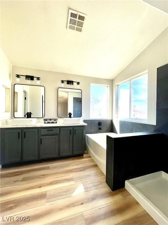 bathroom featuring lofted ceiling, a sink, wood finished floors, visible vents, and double vanity