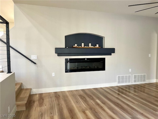 unfurnished living room with baseboards, visible vents, a glass covered fireplace, wood finished floors, and stairs