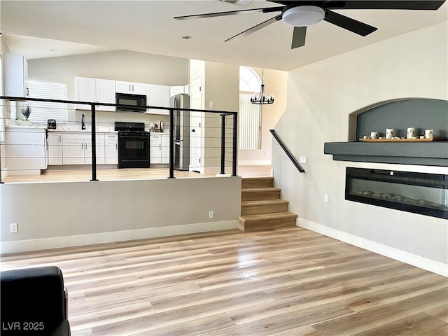 unfurnished living room featuring light wood-style flooring, baseboards, vaulted ceiling, stairs, and a glass covered fireplace