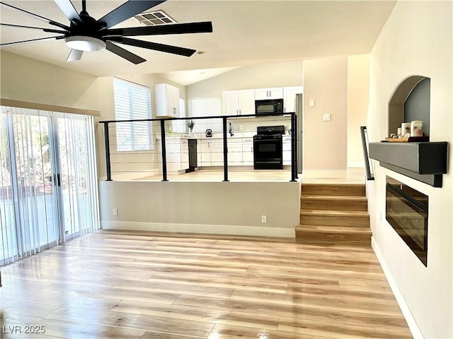 interior space featuring visible vents, baseboards, lofted ceiling, light wood-style flooring, and ceiling fan