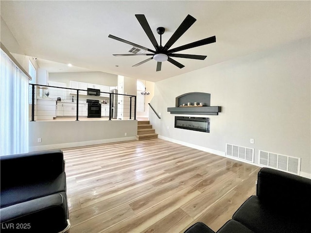 living room with light wood finished floors, lofted ceiling, a glass covered fireplace, baseboards, and stairs