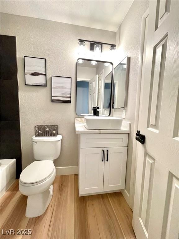 bathroom featuring a textured wall, toilet, wood finished floors, vanity, and baseboards