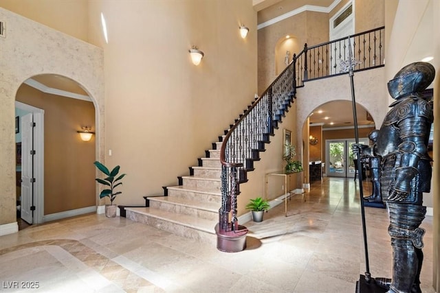 entrance foyer featuring arched walkways, crown molding, a high ceiling, baseboards, and stairs