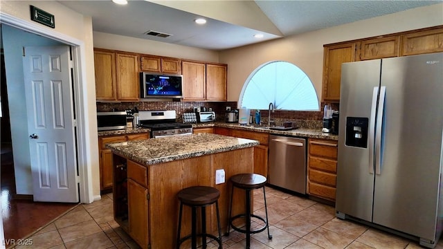 kitchen with stainless steel appliances, a sink, visible vents, a center island, and dark stone counters