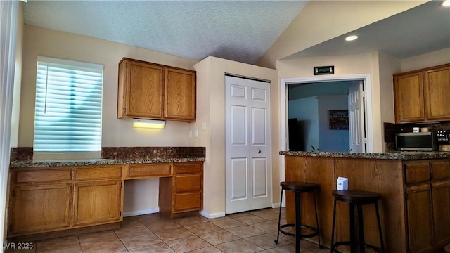 kitchen with brown cabinetry, built in study area, lofted ceiling, a breakfast bar area, and a textured ceiling