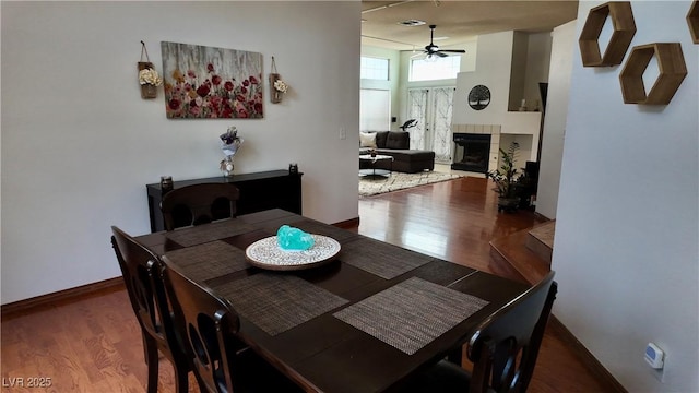 dining room with a fireplace, visible vents, a ceiling fan, wood finished floors, and baseboards