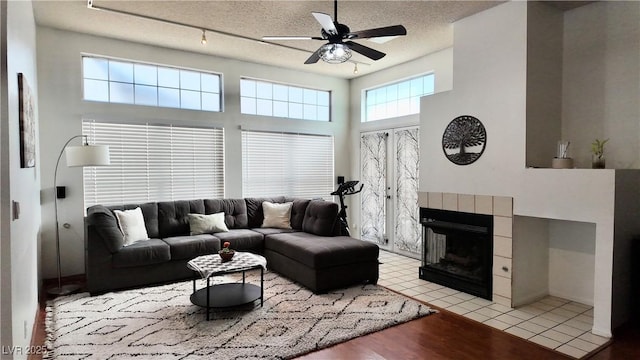 living area featuring a ceiling fan, a fireplace, a textured ceiling, and a high ceiling