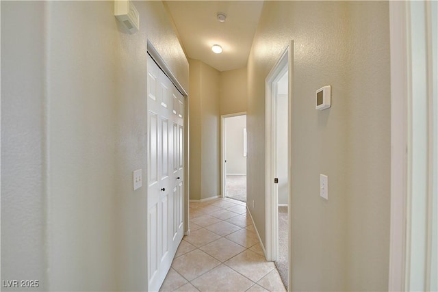 hall featuring light tile patterned flooring and baseboards