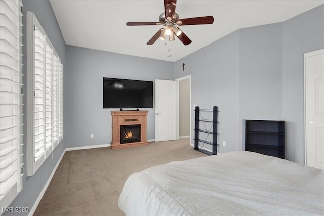 bedroom with light carpet, a lit fireplace, multiple windows, and baseboards