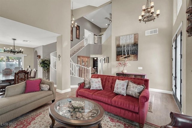 living room featuring a notable chandelier, a high ceiling, wood finished floors, visible vents, and stairs