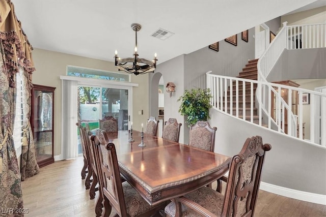 dining area with arched walkways, an inviting chandelier, wood finished floors, baseboards, and stairs