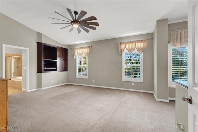 spare room with a ceiling fan, light carpet, vaulted ceiling, and baseboards