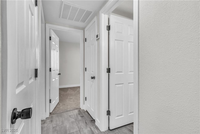 corridor with visible vents, a textured wall, and baseboards