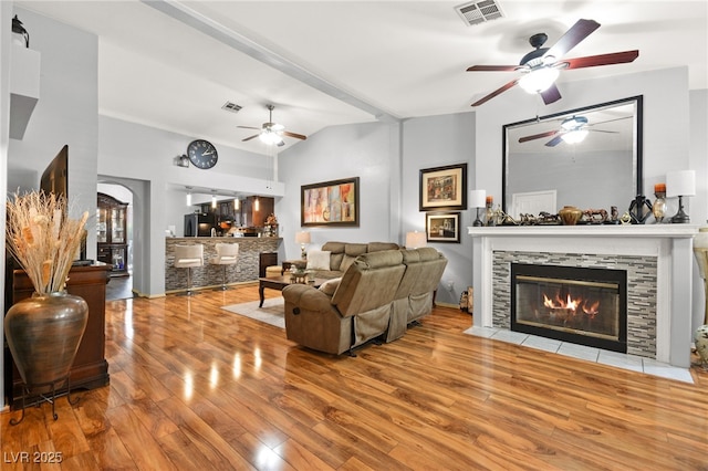 living area featuring lofted ceiling, a stone fireplace, light wood-style flooring, and visible vents