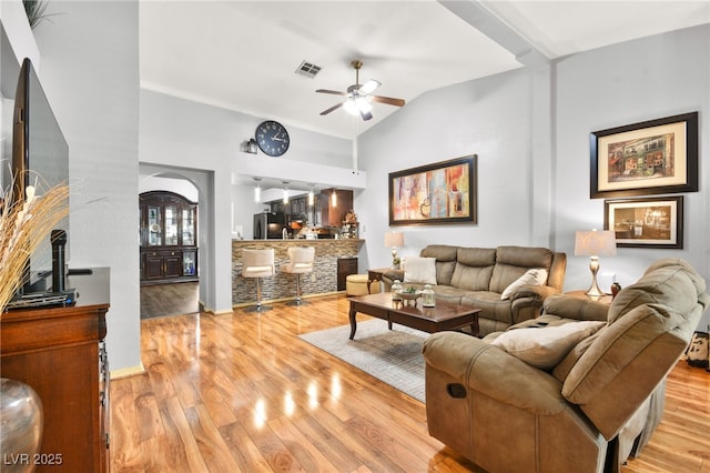 living area featuring a ceiling fan, visible vents, vaulted ceiling, light wood-style floors, and a bar