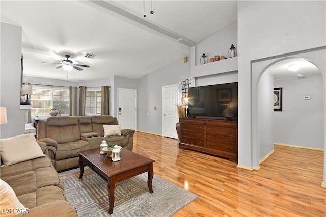 living area with visible vents, arched walkways, a ceiling fan, lofted ceiling with beams, and light wood-style flooring