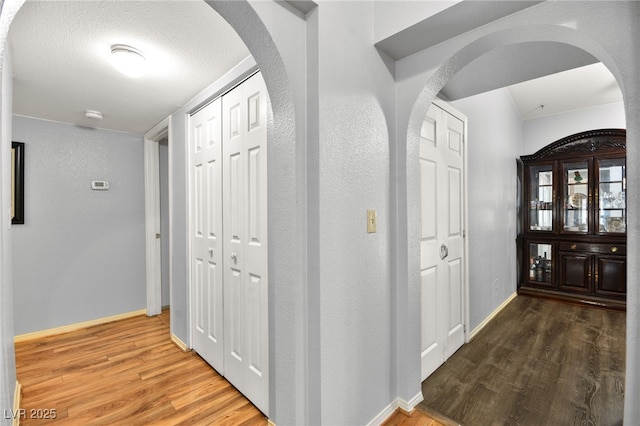 hallway with arched walkways, a textured ceiling, wood finished floors, and baseboards